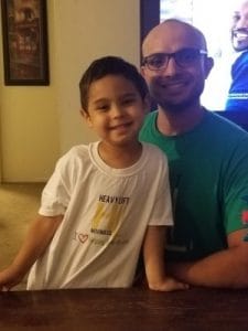 Child wearing a Heavy Lift Moving Co. shirt smiling with family at home